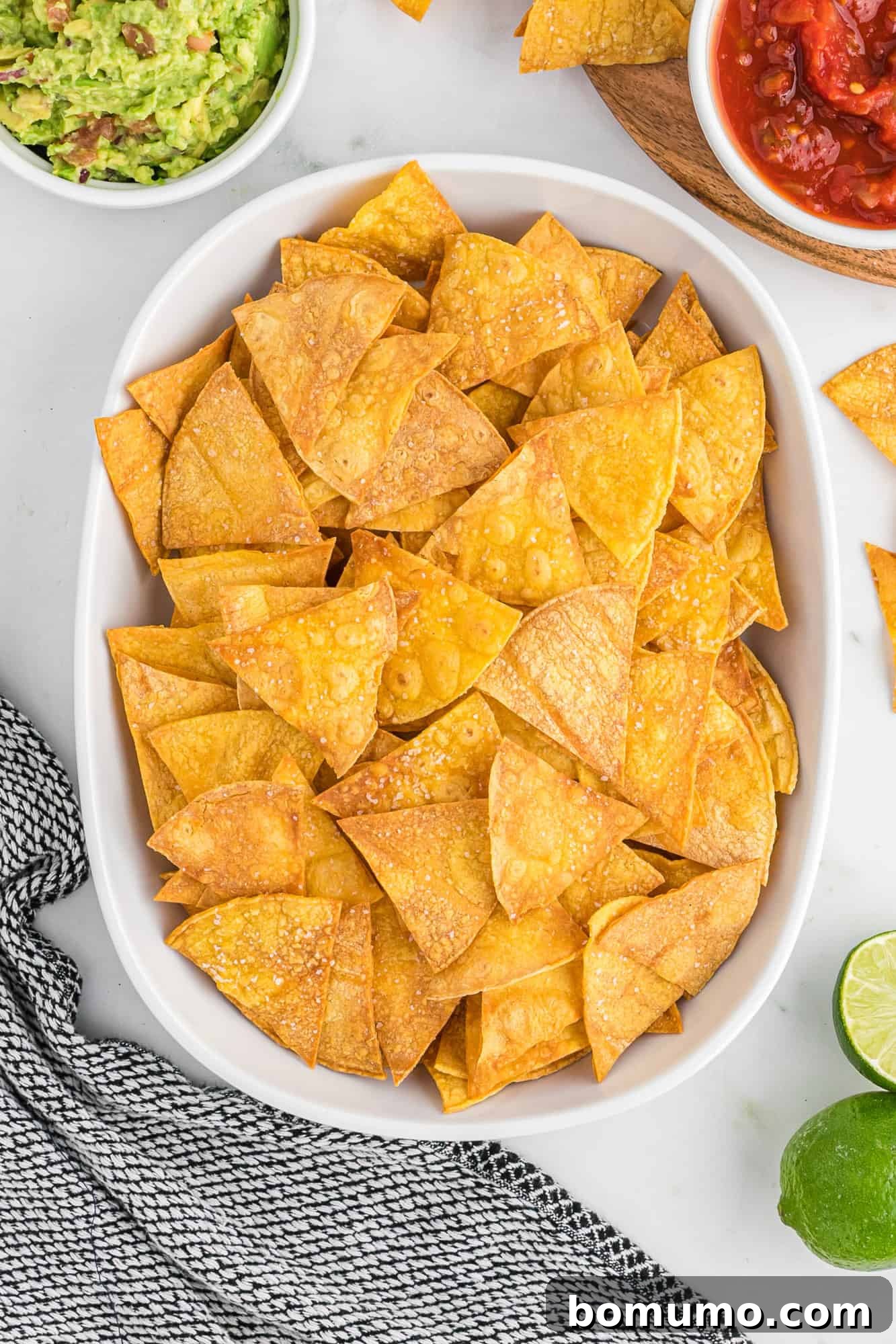 Corn-tortilla-chips A large white serving dish overflowing with perfectly golden-brown baked tortilla chips, ready for a gathering.