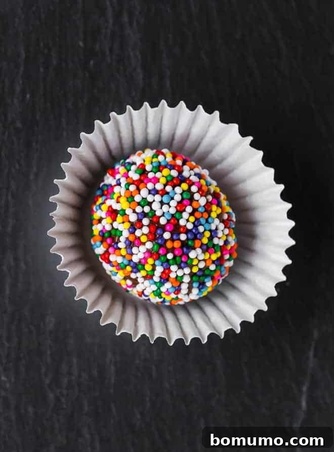 A close-up image of a perfectly round brigadeiro, coated in a vibrant mix of colorful sprinkles, ready to be enjoyed.