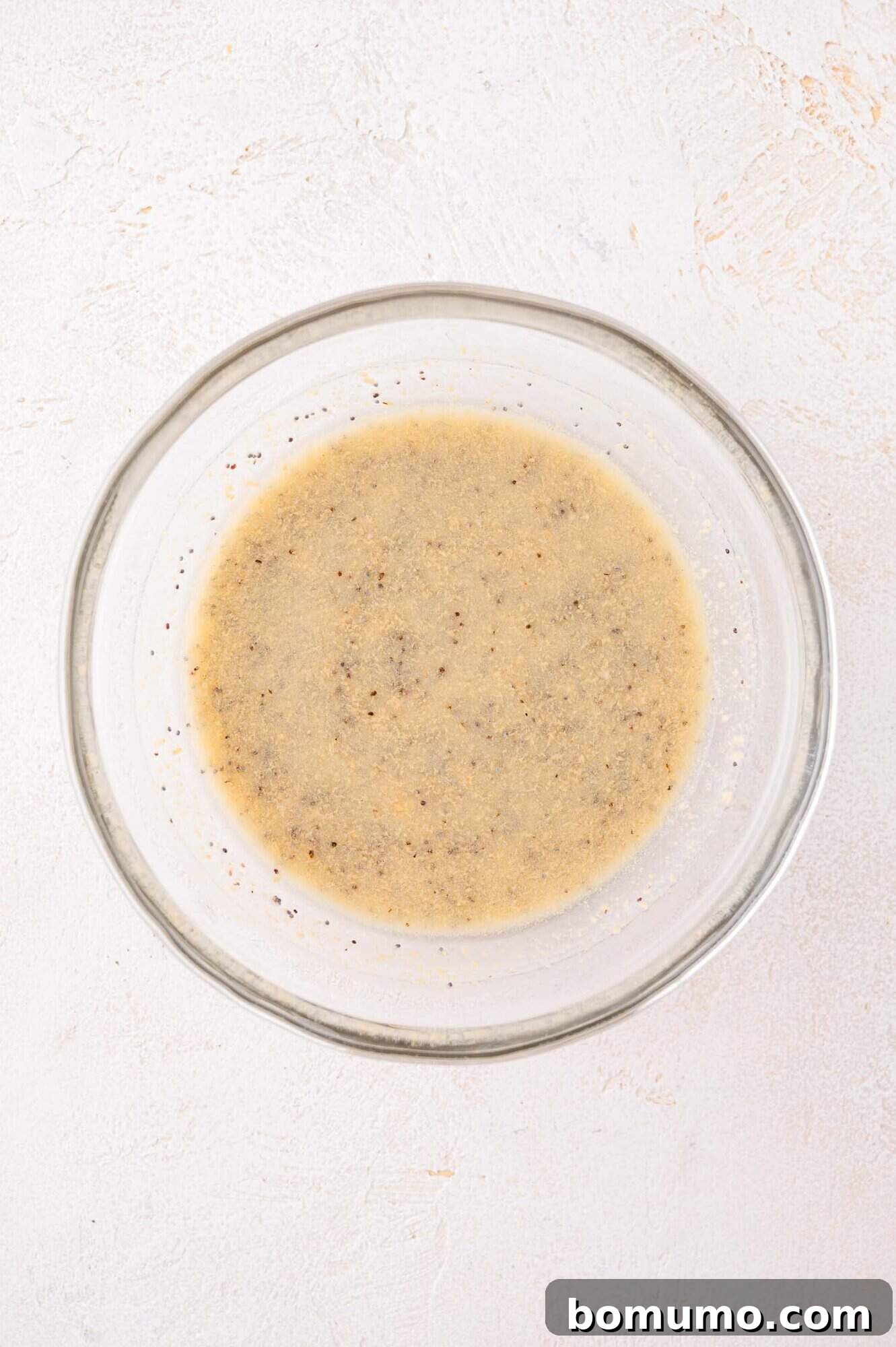 A clear glass bowl containing butter mixture on a light textured surface.