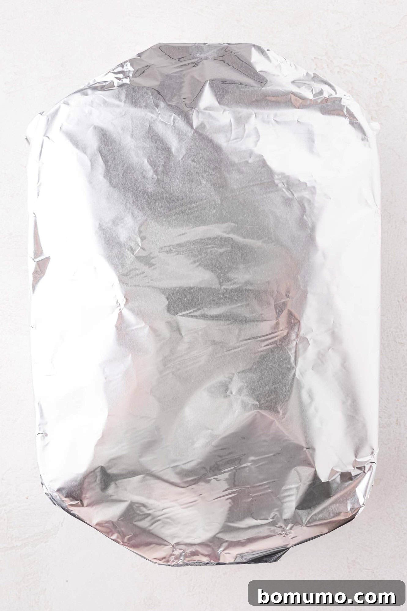 A rectangular baking dish covered with a sheet of aluminum foil, placed on a light-colored surface.