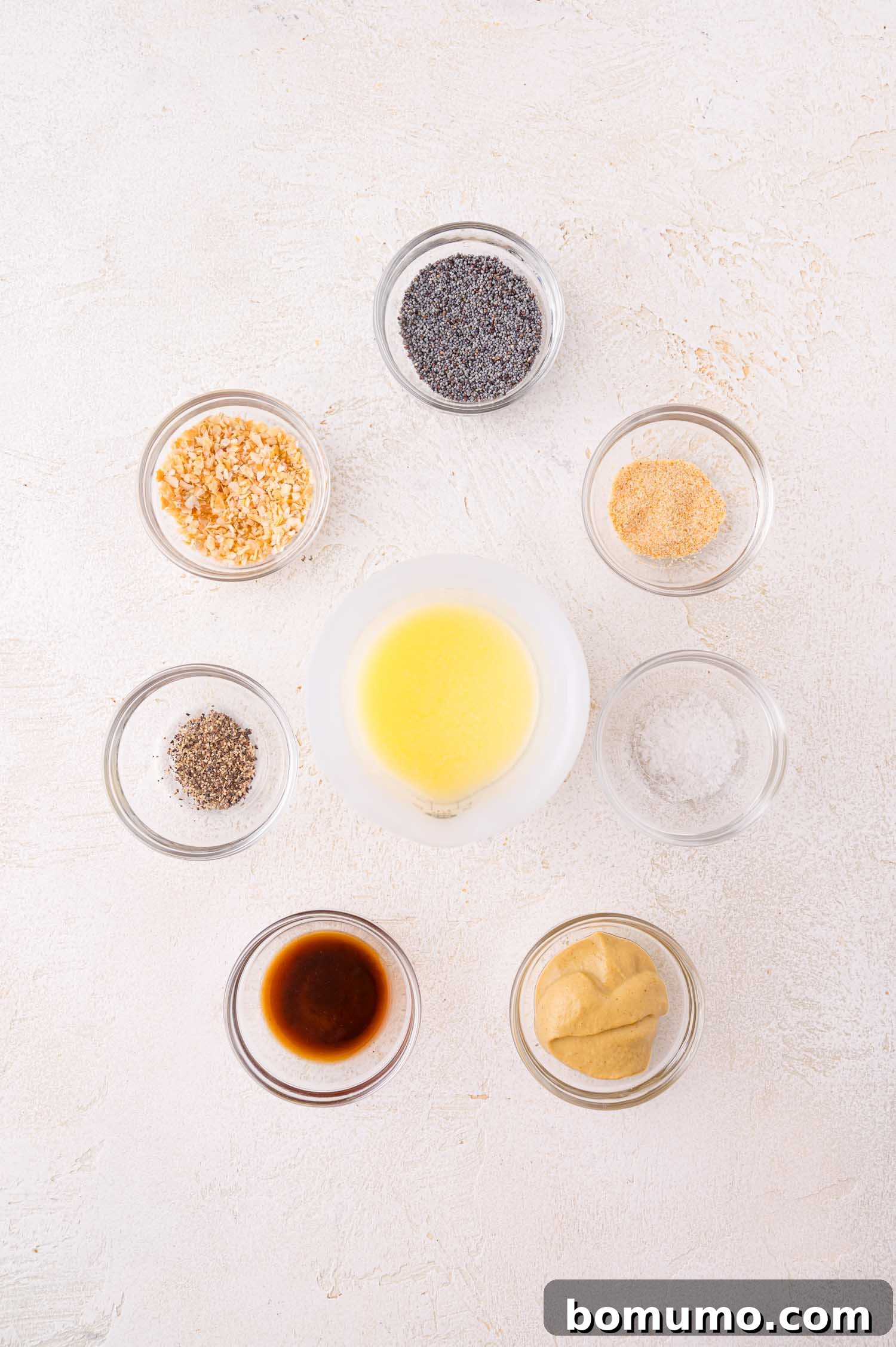 Eight small bowls containing ingredients for the topping arranged on a white surface.