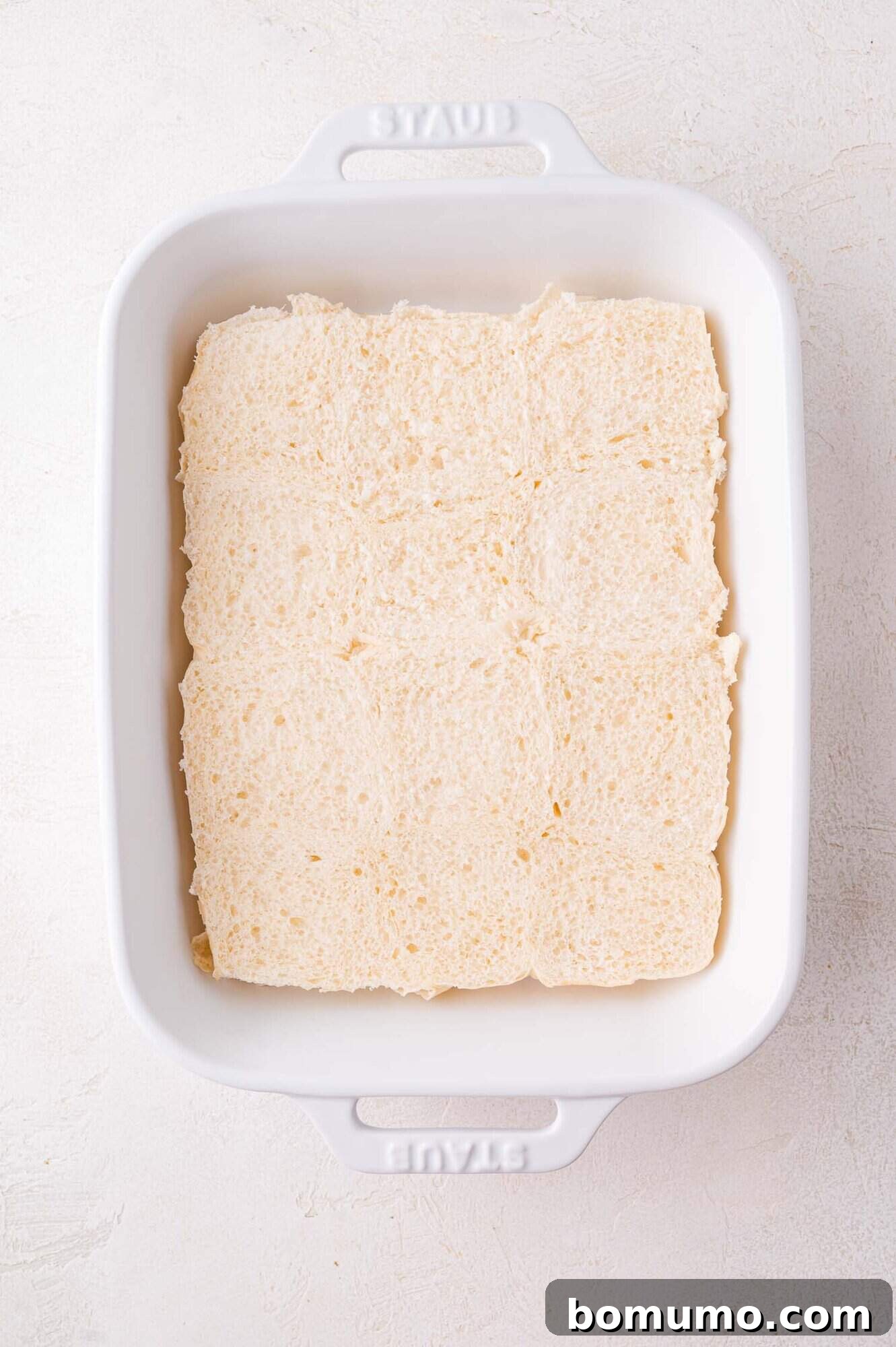 Slider roll bottom halves arranged in a single layer to cover the bottom of a white rectangular baking dish.