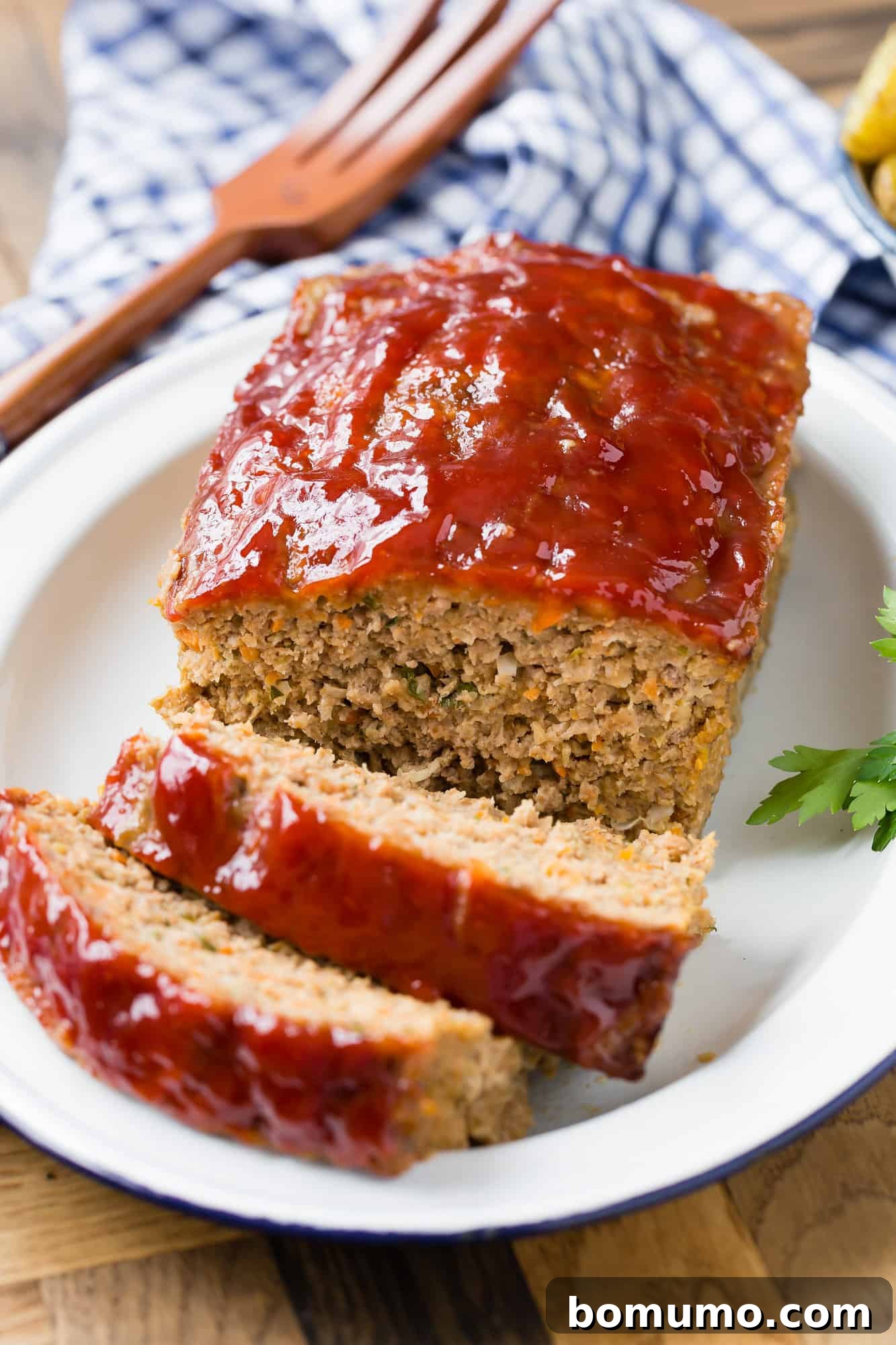Homemade meatloaf on a platter, partially sliced, showcasing its perfect golden-brown crust and juicy interior.