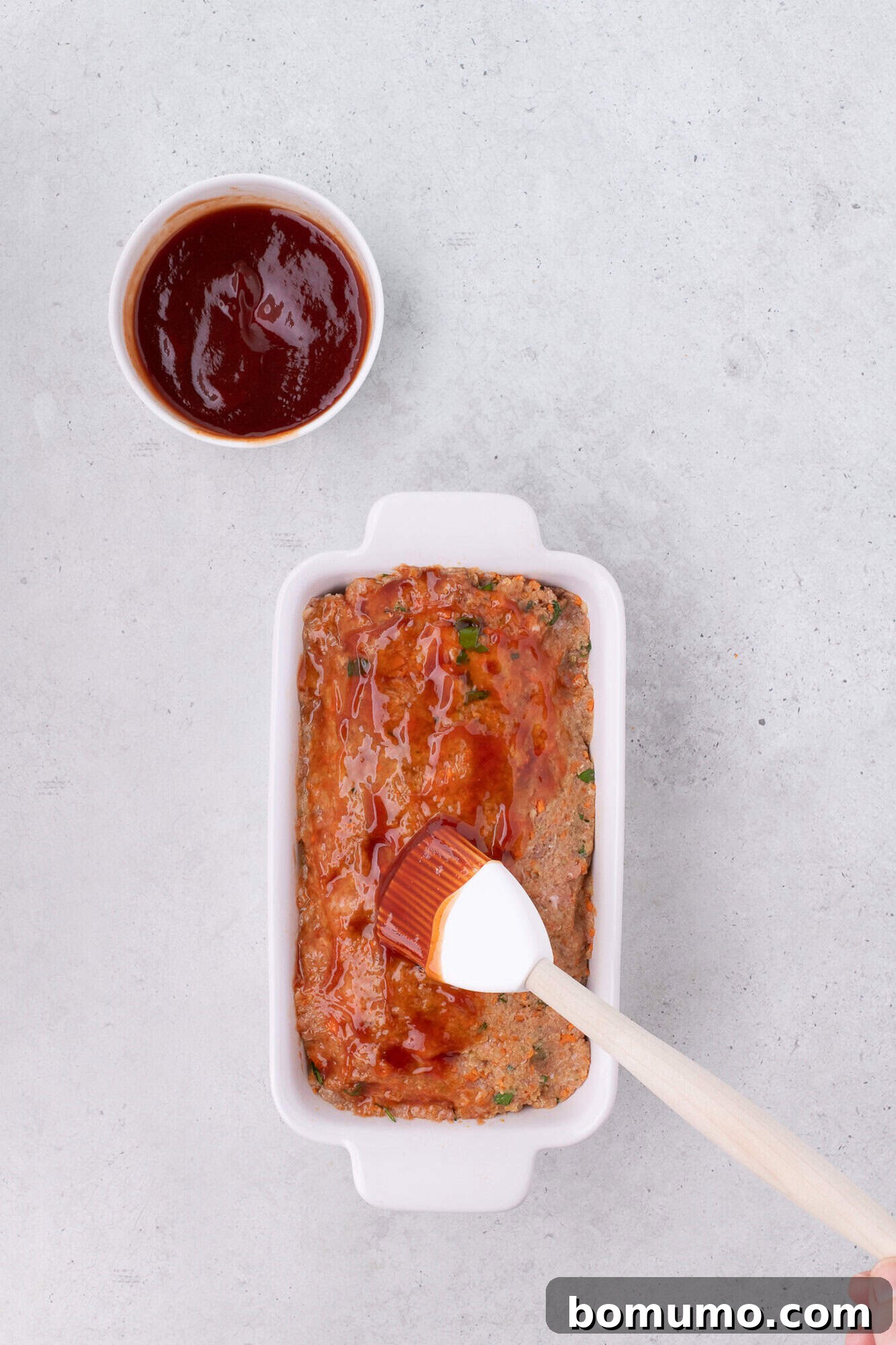The tangy tomato glaze being evenly spread over the unbaked meatloaf surface.