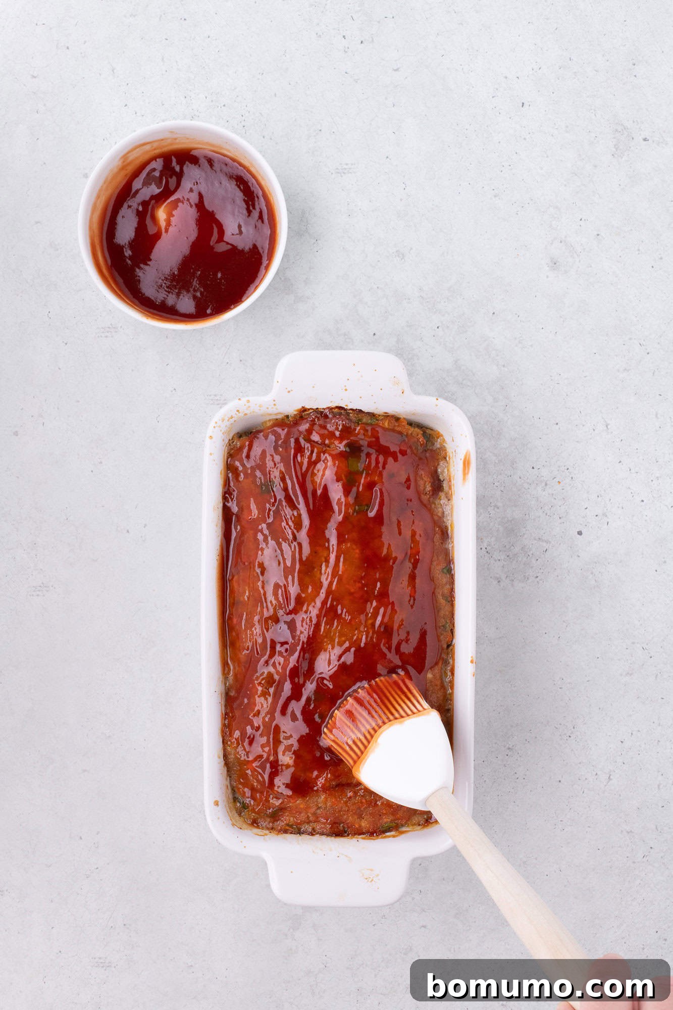 The second layer of tangy glaze being artfully spread over the partially baked meatloaf.
