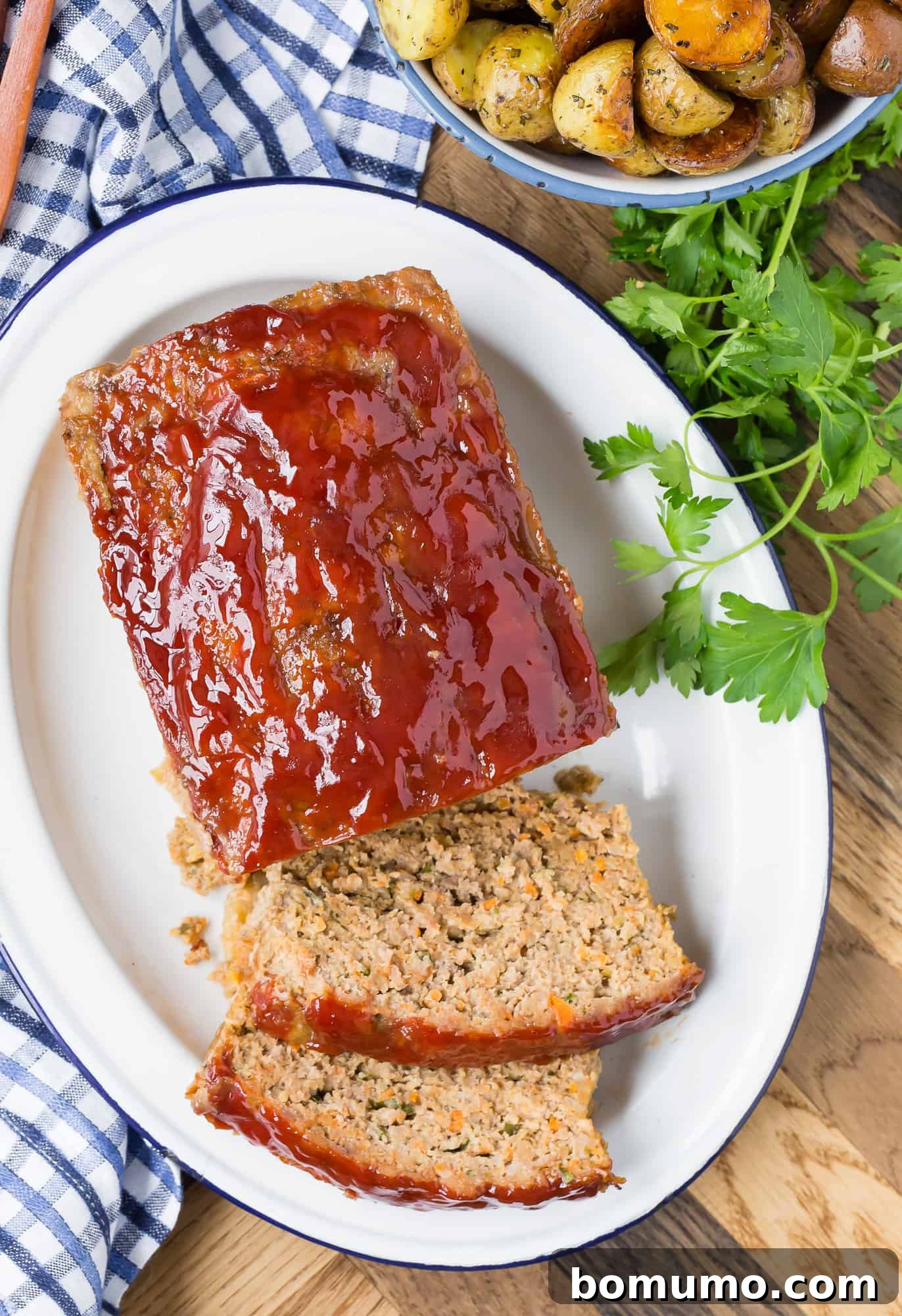 Overhead view of a perfectly baked meatloaf, partially sliced to reveal its tender texture, glistening with a vibrant tomato glaze.