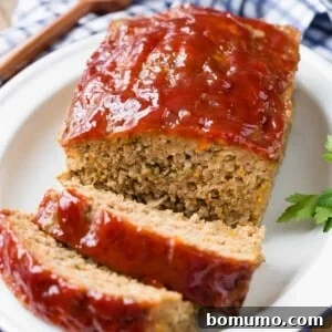 Homemade meatloaf on a platter, partially sliced, showcasing its perfect golden-brown crust and juicy interior.