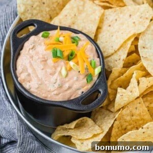 Image of mexicali dip in a black bowl with two handles. Dip is surrounded by chips on a tray.