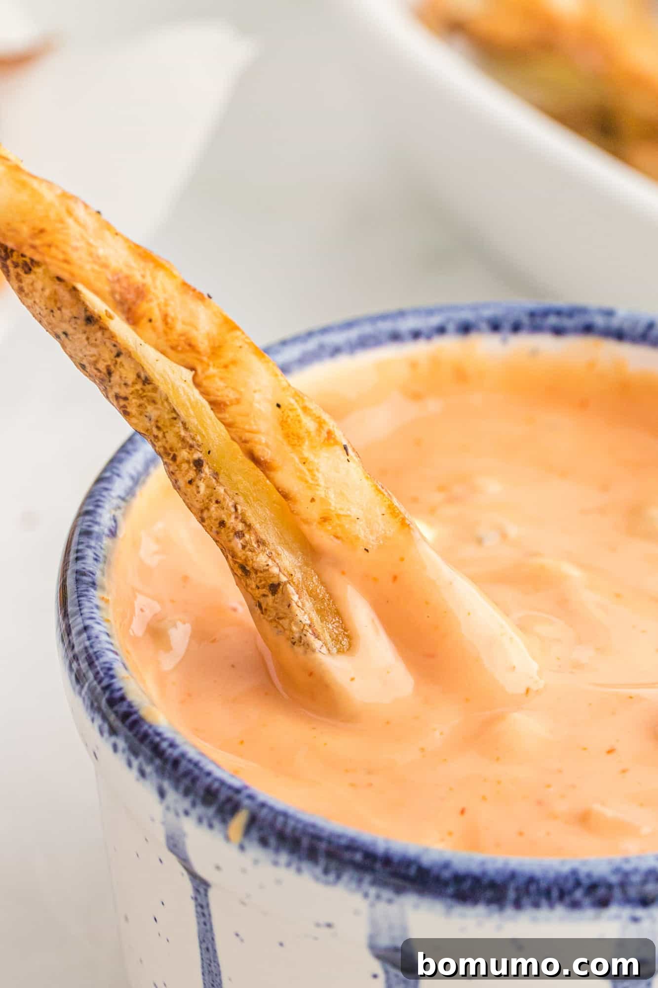 Crispy French fries being dipped into a small bowl of creamy, light orange fry sauce, showcasing its inviting texture.