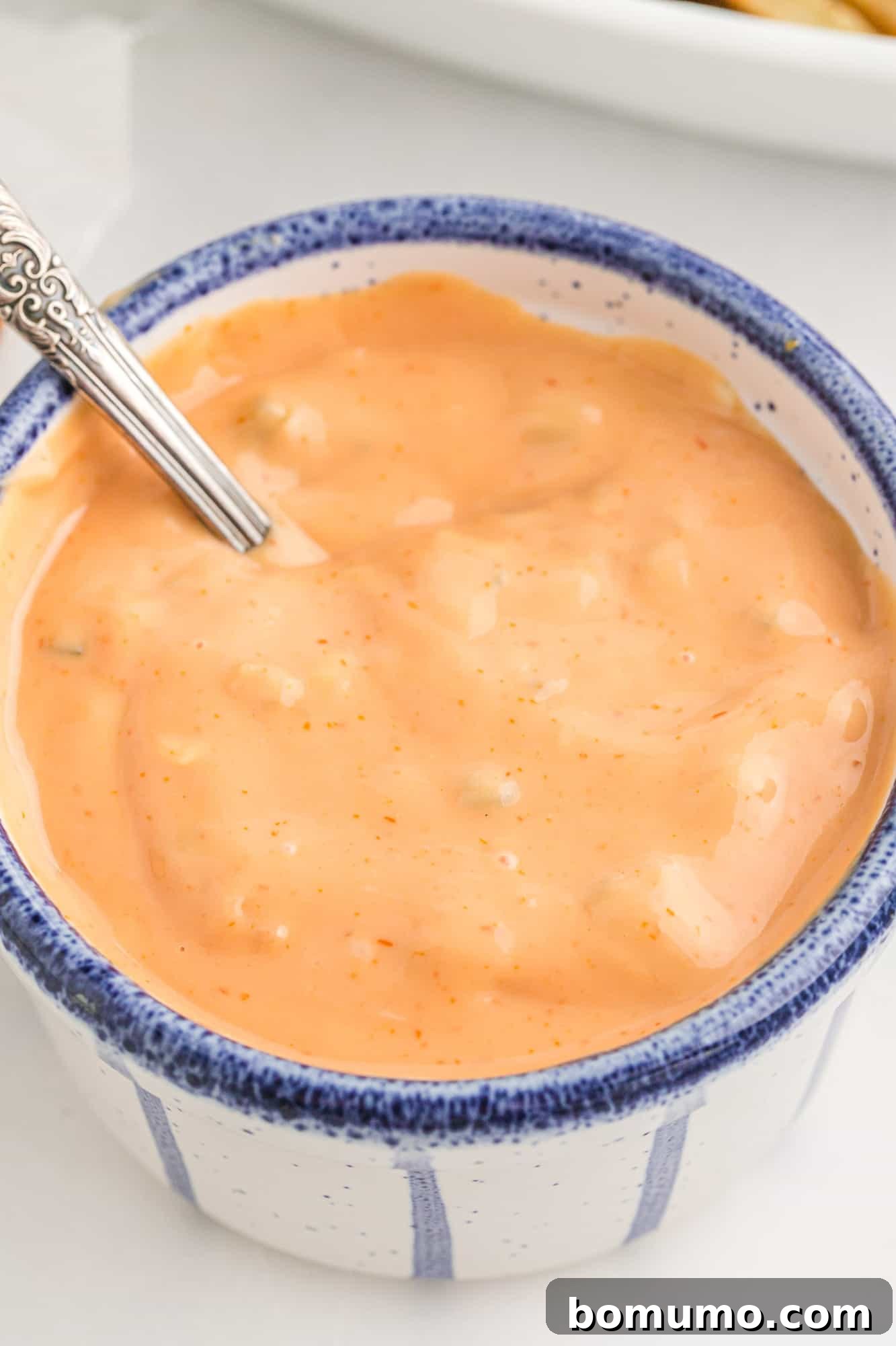 A small, elegant blue and white bowl filled with creamy, light orange fry sauce, ready for dipping.