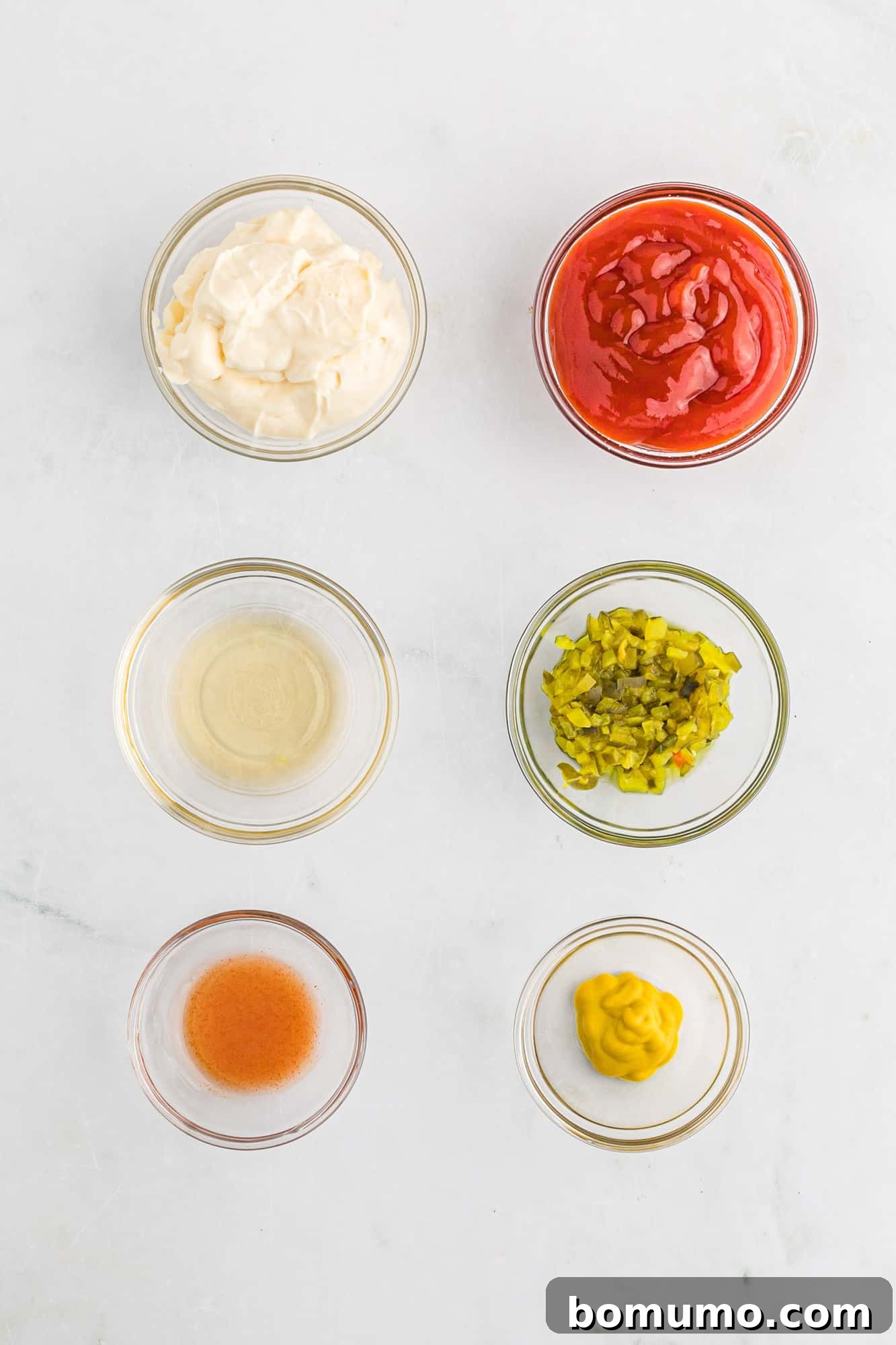 Individual small glass bowls holding the key ingredients for fry sauce: mayonnaise, ketchup, dill pickle relish, mustard, and a bottle of hot sauce.