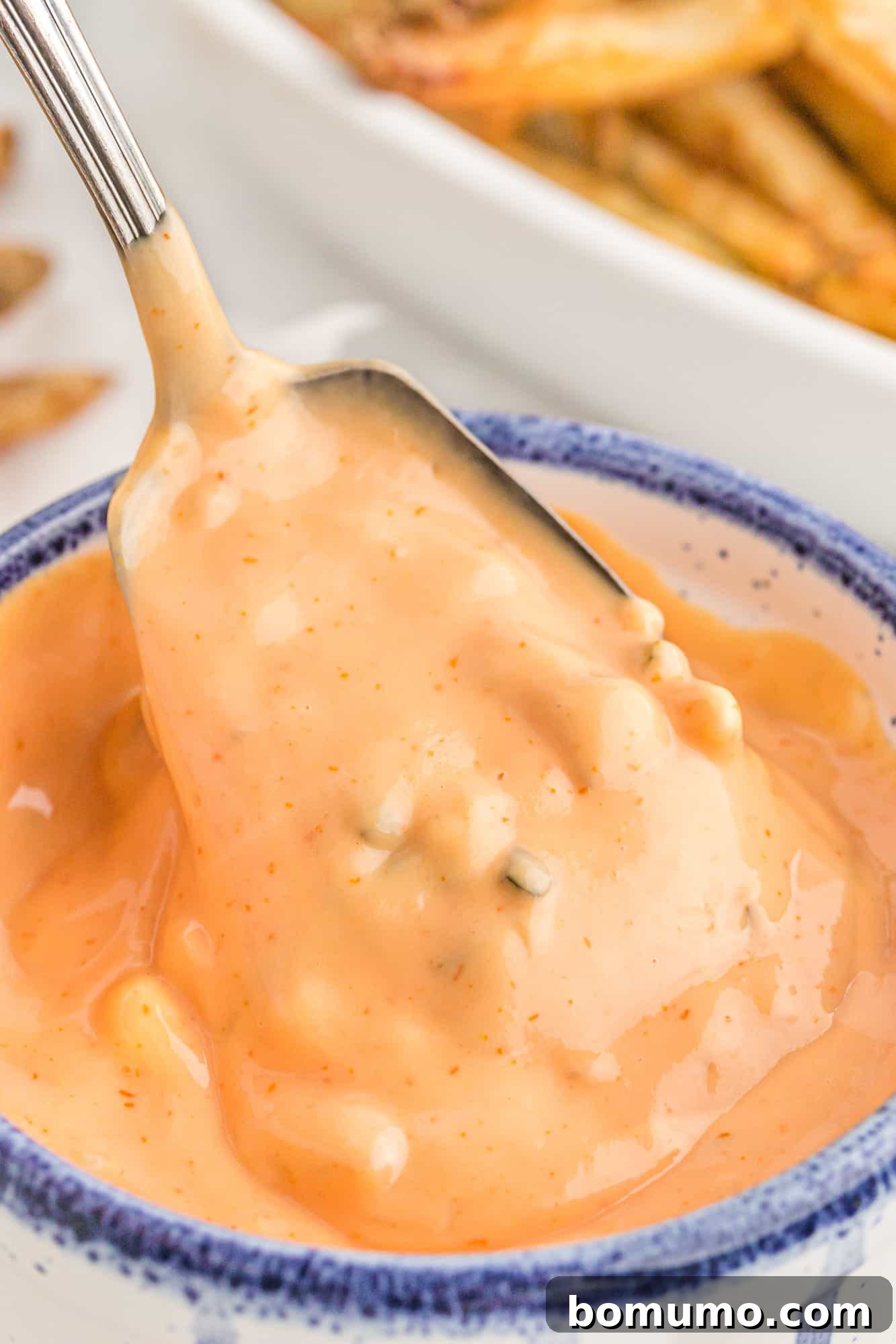 A close-up of the light orange fry sauce in a bowl, showing its creamy texture with subtle specks of pickle relish.