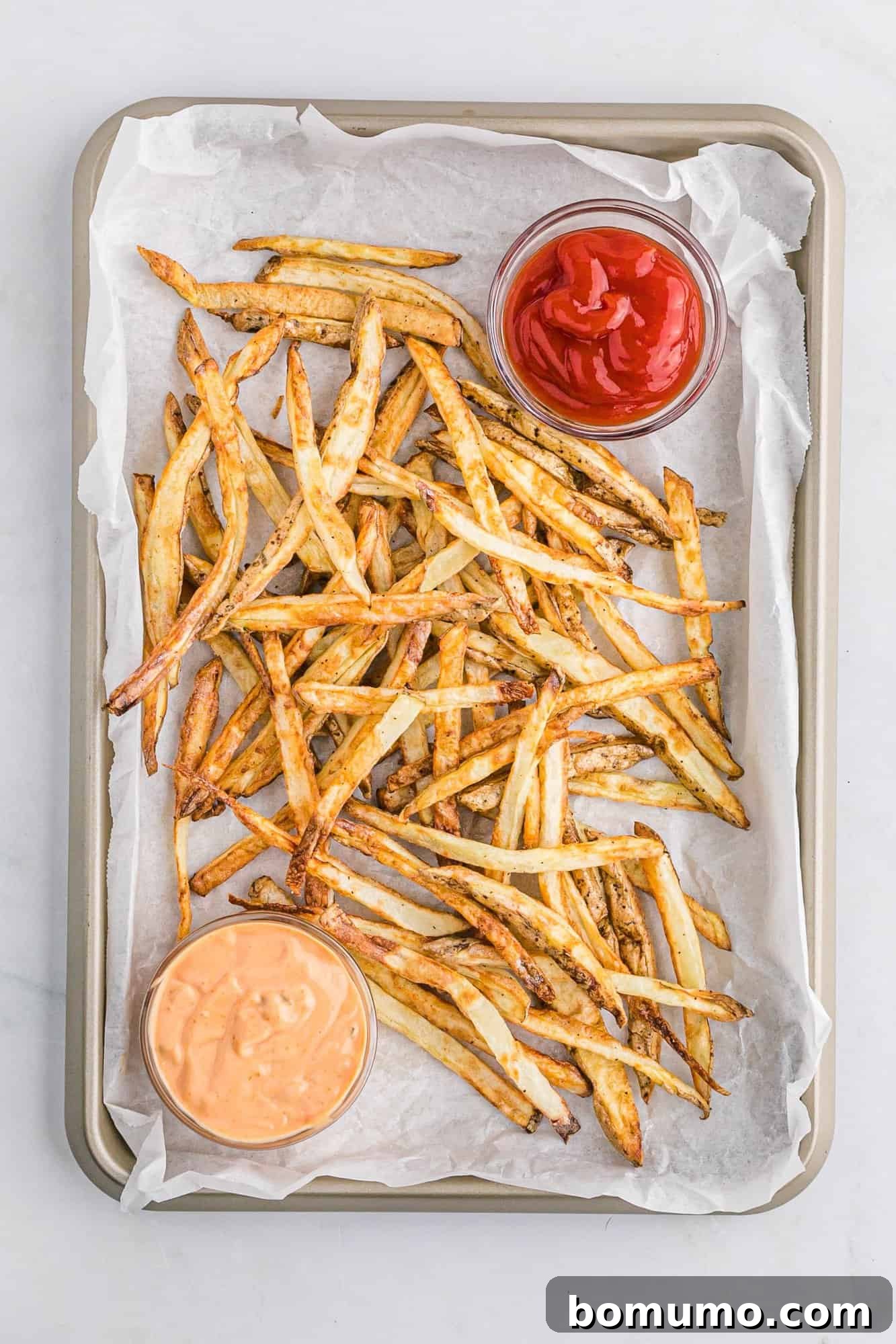 Overhead view of crispy air fryer French fries served in a bowl with two dipping sauces, highlighting their golden perfection and appetizing appeal.