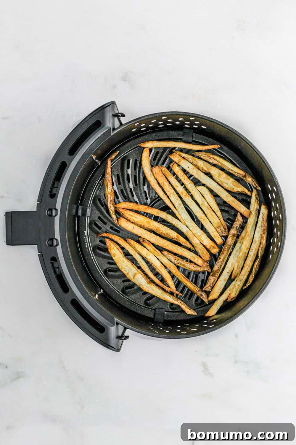 Thin, golden-brown and perfectly crispy fries displayed in an air fryer basket, fresh from cooking.