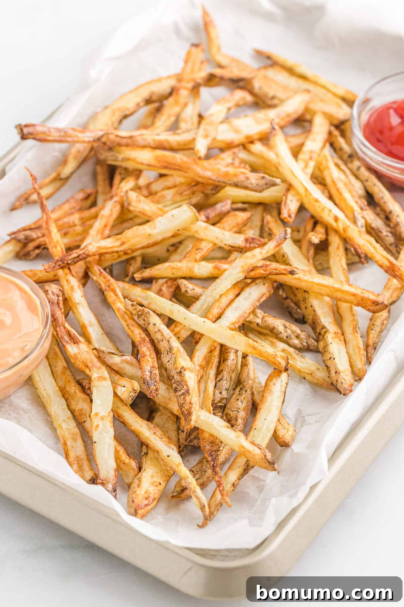 Crispy golden air fryer French fries scattered on a parchment-lined baking sheet, ready for serving or further seasoning.
