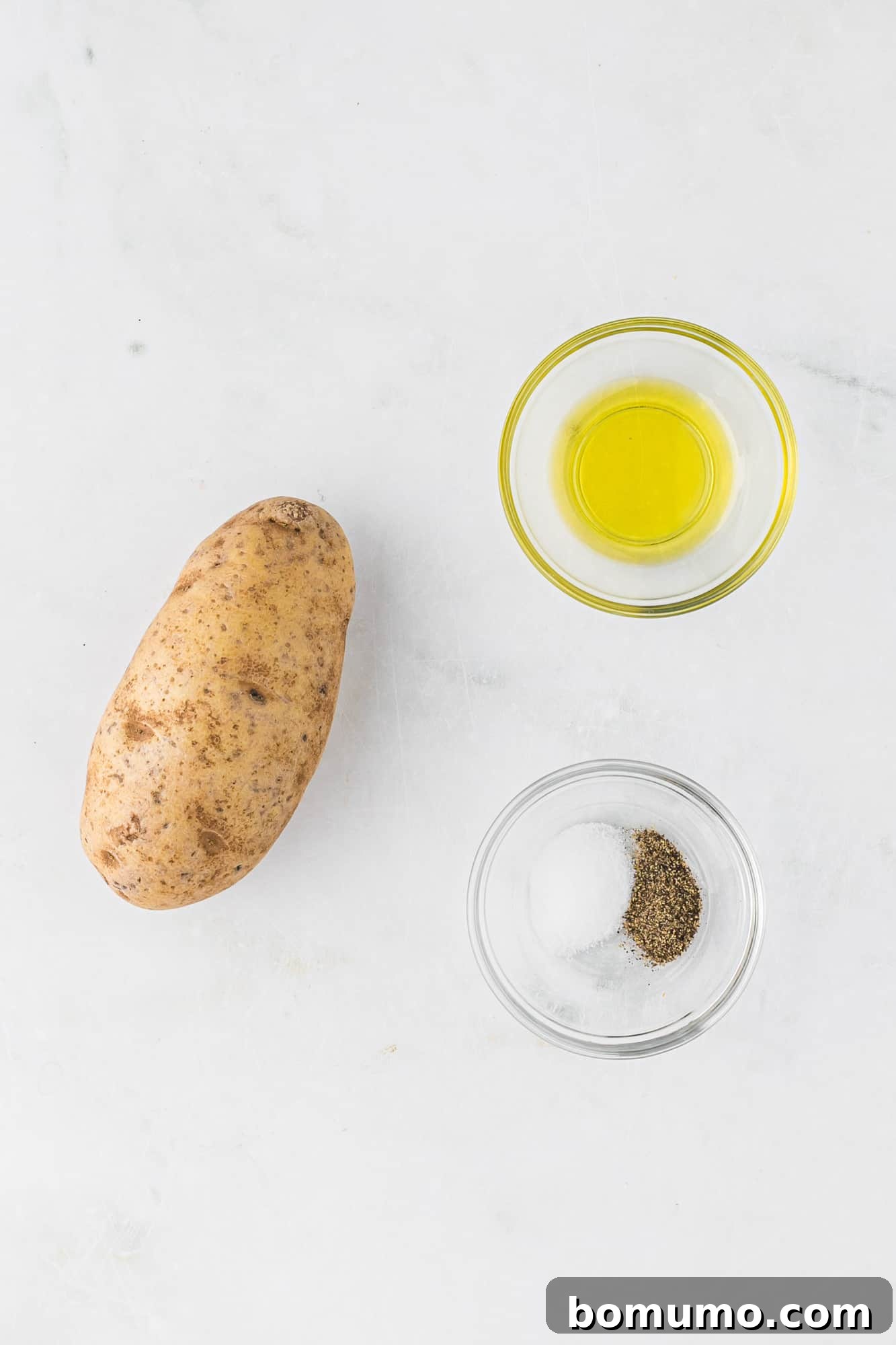 Ingredients needed for air fryer fries: a whole potato, olive oil, salt, and pepper arranged on a wooden board.
