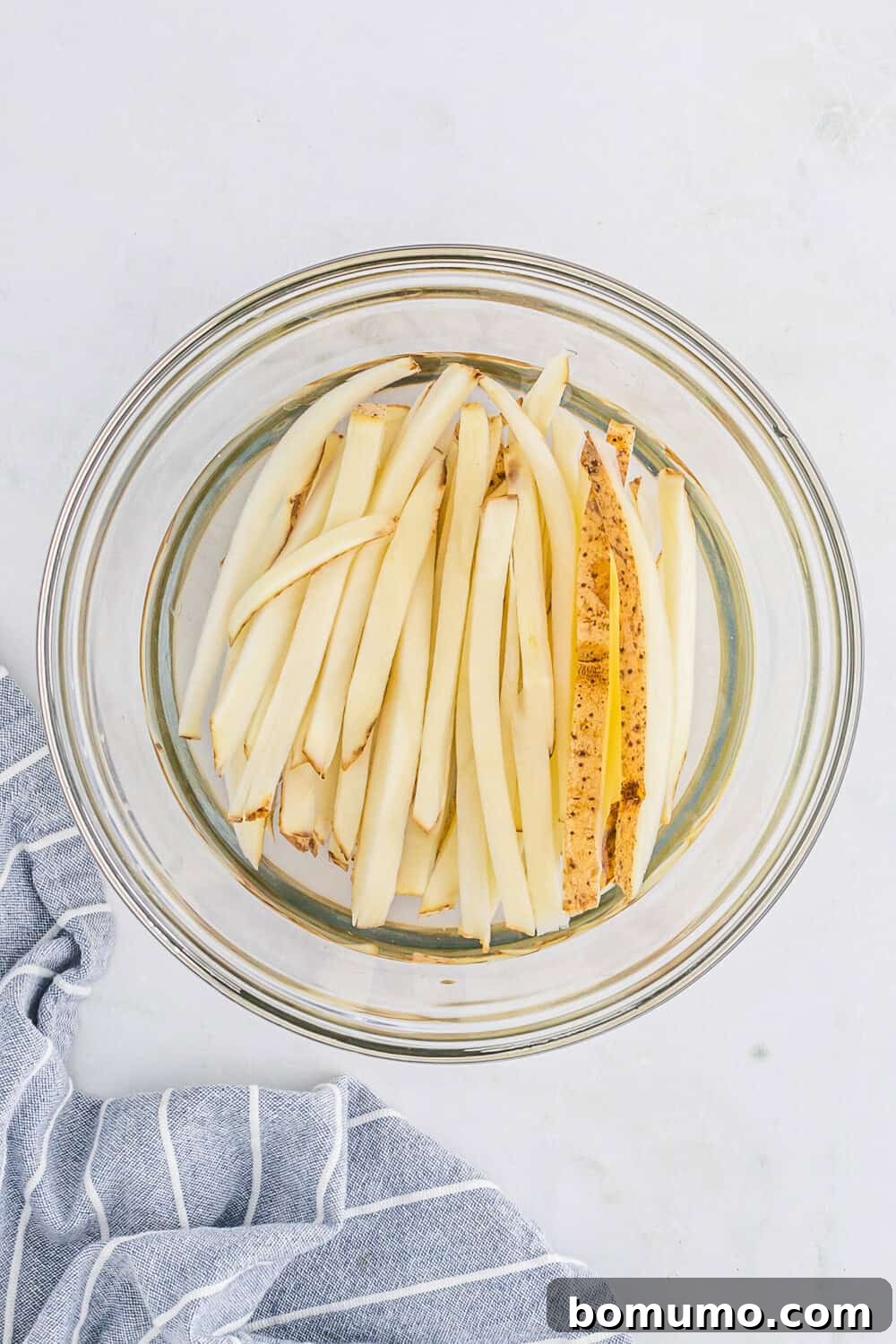 Potato slices soaking in cold water in a clear glass bowl, a vital step for achieving crispy air fryer fries.