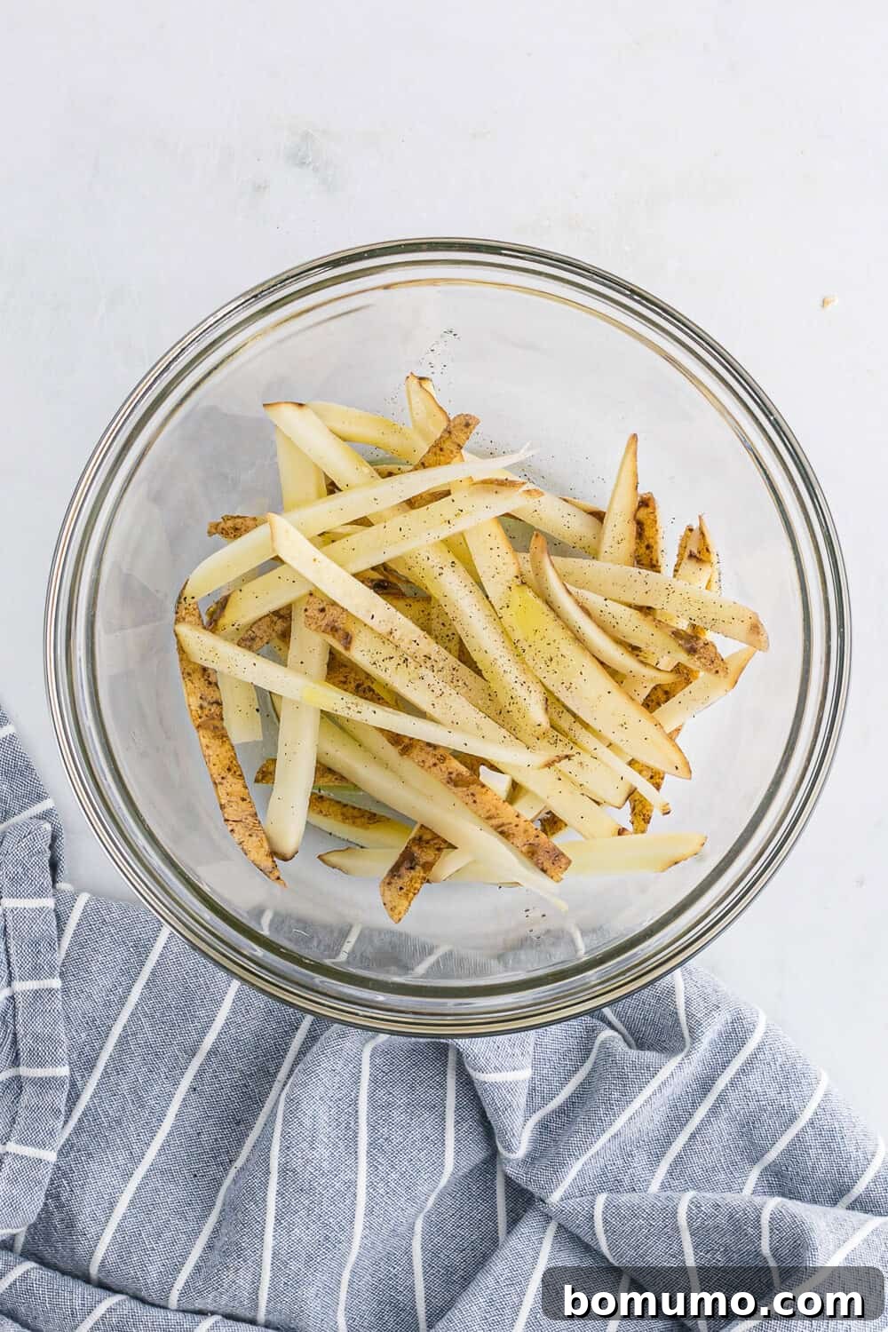 Potato slices seasoned with salt and pepper in a glass bowl, perfectly coated and ready for the air fryer.