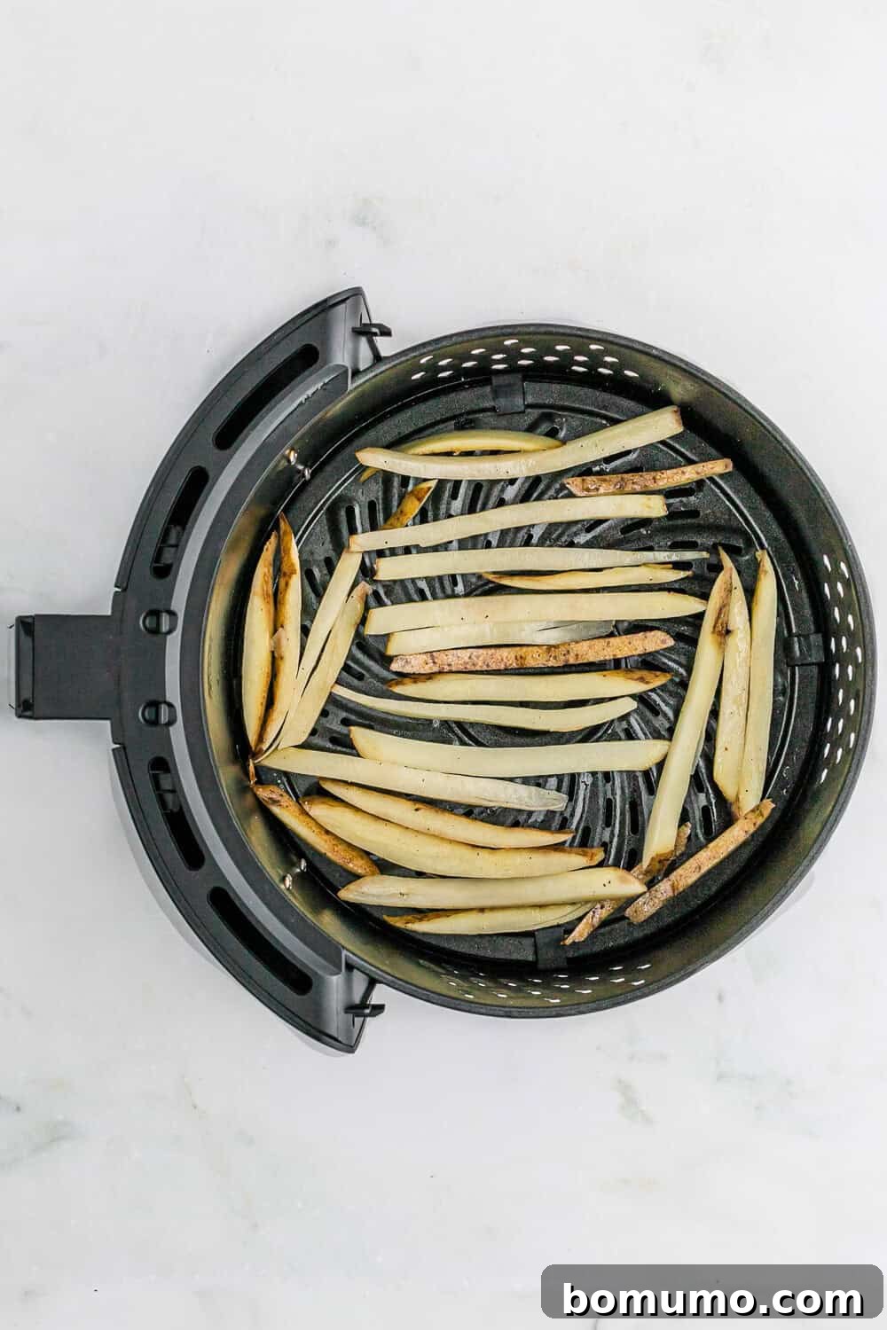 Sliced potatoes arranged in a single, uncrowded layer inside an air fryer basket, demonstrating ideal spacing for even crisping.