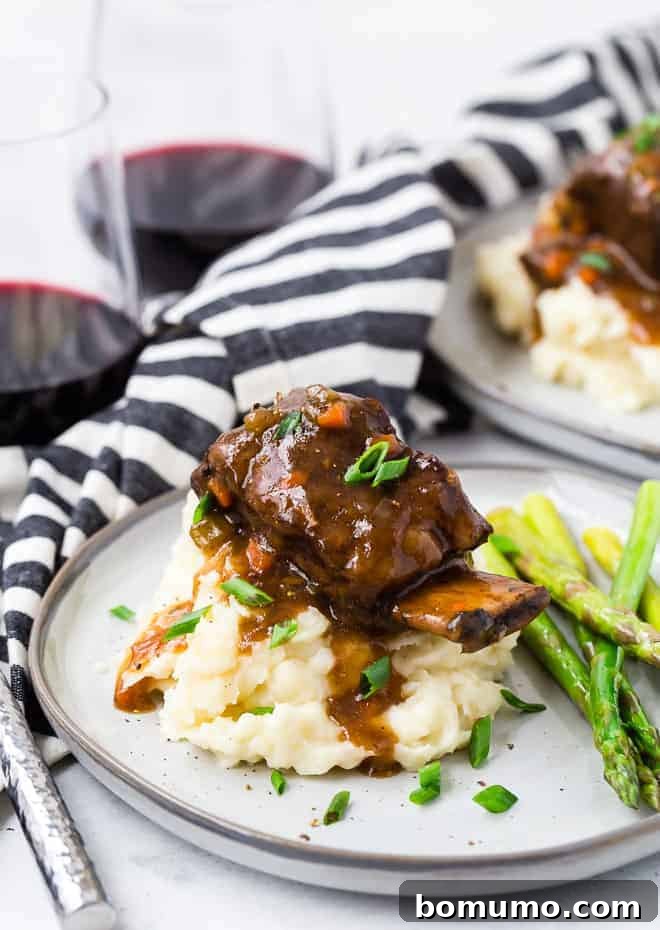 Image of Instant Pot short ribs on a pile of mashed potatoes, garnished with fresh chives. Short ribs are served with sauteed asparagus and a glass of red wine.