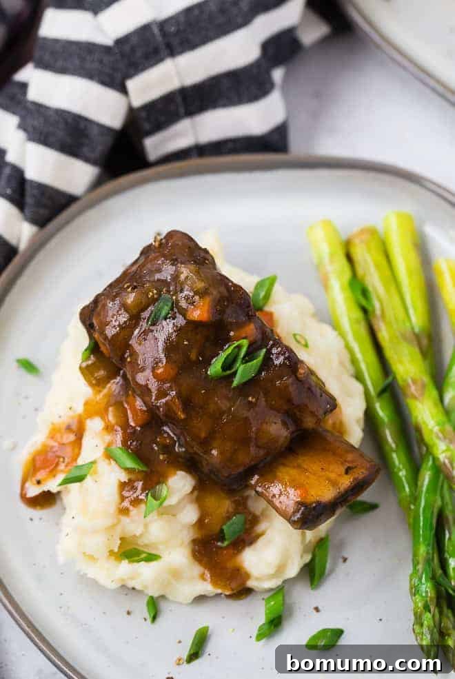 Image of a cooked short rib and gravy atop a pile of creamy mashed potatoes.