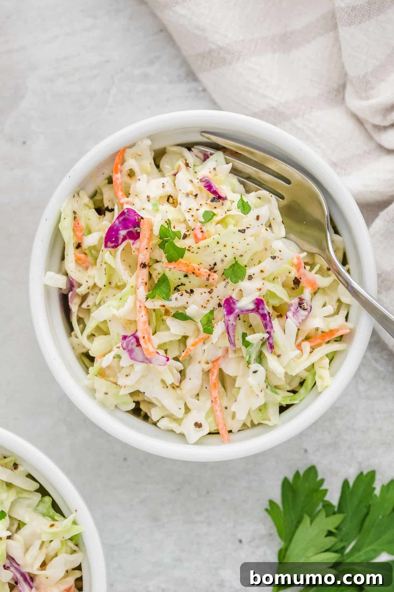 Overhead view of healthy coleslaw in a small round bowl, garnished with fresh parsley.