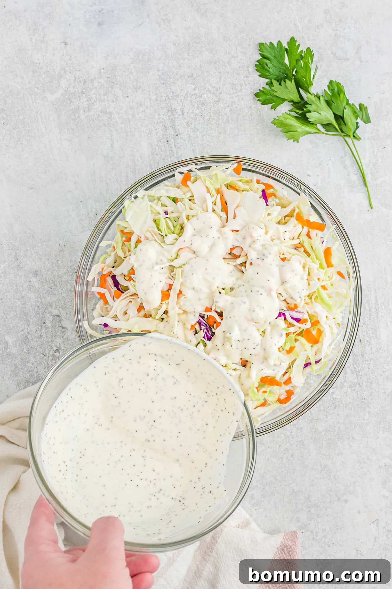Coleslaw dressing being poured onto shredded cabbage and carrots in a large mixing bowl.