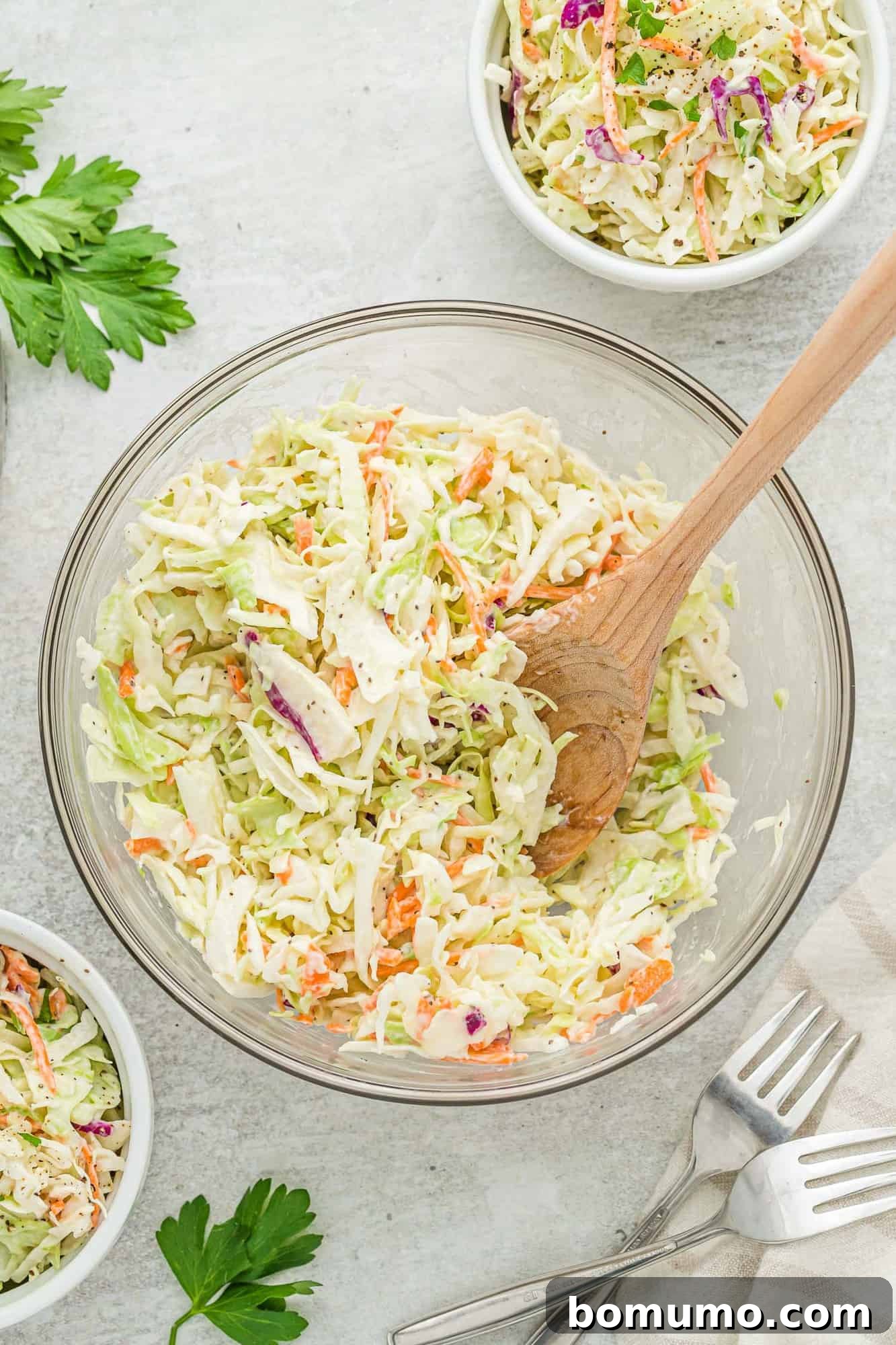 Finished coleslaw in a large mixing bowl with a wooden spoon, ready for chilling.