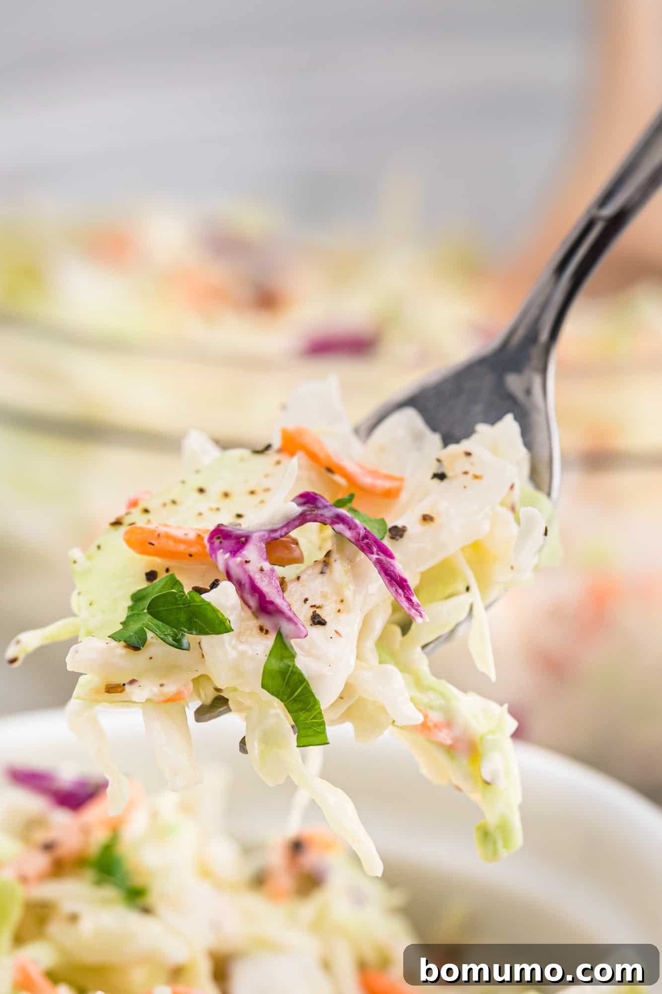 Coleslaw on a fork, showing individual components of cabbage and carrots coated in dressing.