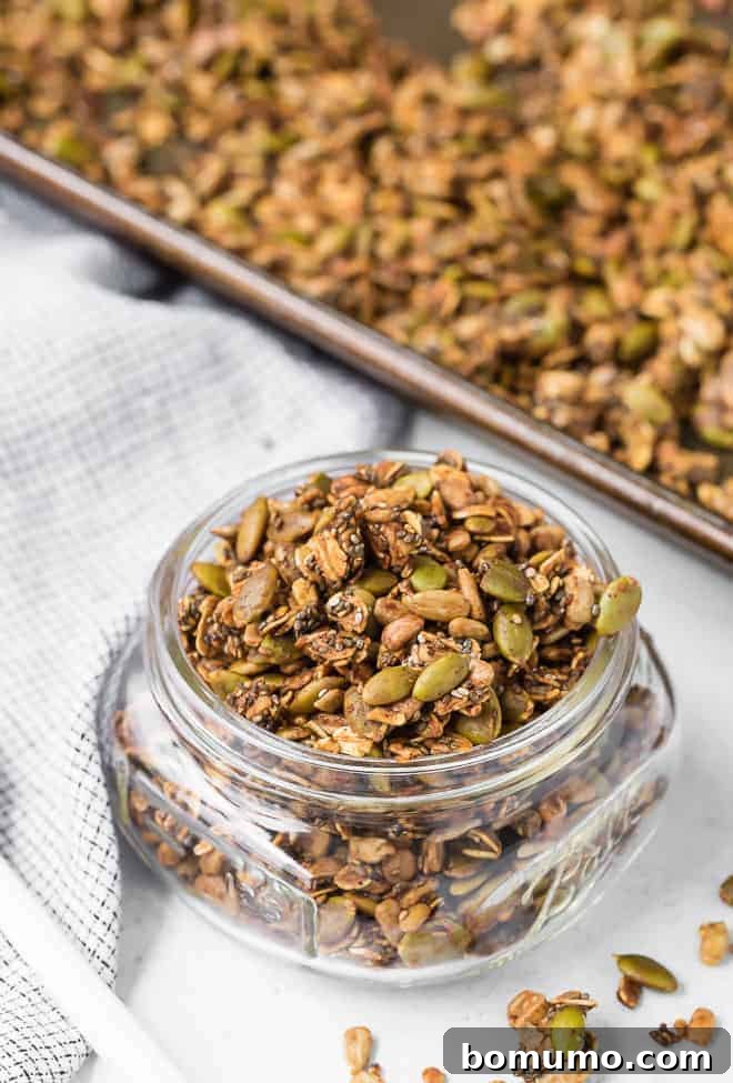 Image of savory granola in a jar, spilling out. A pan of granola is also pictured in the background, hinting at its homemade goodness and abundance.