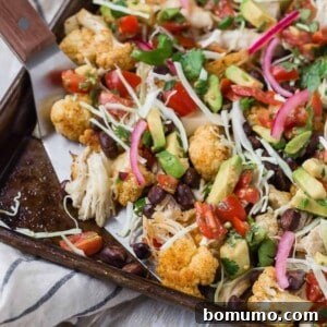 Cauliflower nachos on a sheet pan with colorful toppings.