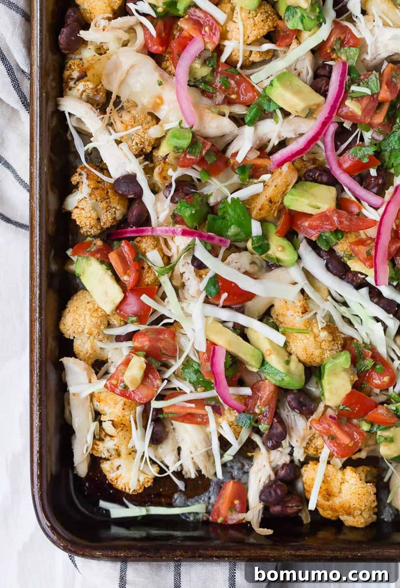 Supreme Cauliflower Nachos 4 A colorful array of cauliflower nachos arranged on a sheet pan with various fresh toppings, ready to be served.