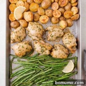 Sheet pan with roasted chicken thighs, halved potatoes, and green beans, garnished with fresh lemon wedges.