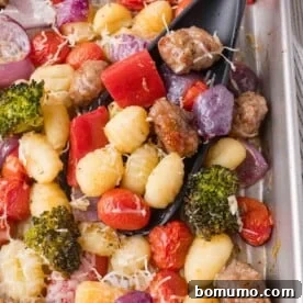A tray of baked gnocchi with Italian sausage, cherry tomatoes, broccoli, red onions, red bell peppers, and grated cheese.