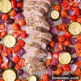 Sliced seasoned pork tenderloin on a baking sheet, surrounded by roasted zucchini, cherry tomatoes, red onion, red bell pepper, and kalamata olives.