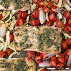 Close up view of perfectly cooked salmon with dill and capers, surrounded by beautifully roasted vegetables like tomatoes and fennel.