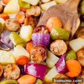 Sliced sausage with a medley of colorful roasted vegetables and potatoes on a sheet pan.