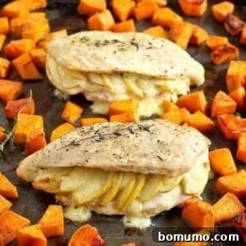 Two generously stuffed chicken breasts on a sheet pan with roasted sweet potatoes.