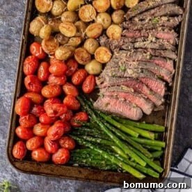 Perfectly cut steak, showing a pink interior, on a sheet pan with roasted tomatoes, potatoes, and asparagus.