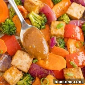 Rich peanut sauce being generously added to a vibrant tofu sheet pan dinner, enhancing its savory appeal.