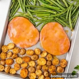 Sheet pan with glazed ham steaks, roasted baby potatoes, and vibrant green beans for a complete meal.