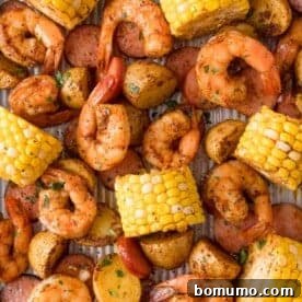A sheet pan filled with cooked shrimp, sliced sausage, corn on the cob, and roasted potatoes, garnished with herbs.