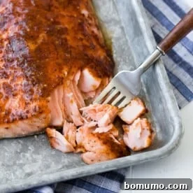 Maple mustard baked salmon on a sheet pan, being flaked with a fork.