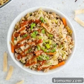 Overhead view of egg roll in a bowl drizzled with sriracha.