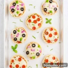 Overhead view of English muffin pizzas on a parchment paper-lined baking sheet, a perfect quick meal or snack.