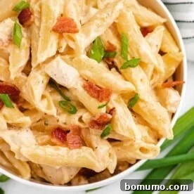 Pasta with chicken, cheese sauce, bacon, and green onions, in a white bowl.