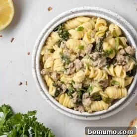 Overhead view of pasta with ground chicken, lemon, and spinach on a white plate.