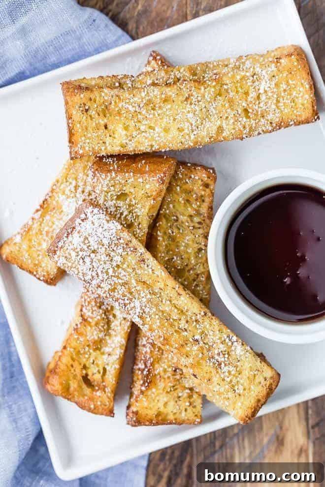 Overhead view of air fryer french toast sticks on a white plate with a bowl of maple syrup for dipping.