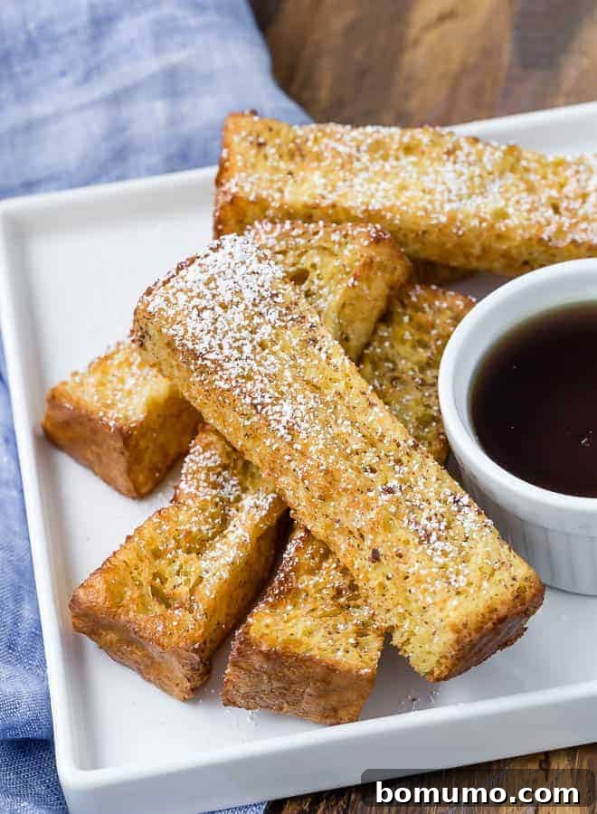 Air fryer french toast sticks on a white plate with a bowl of maple syrup for dipping.