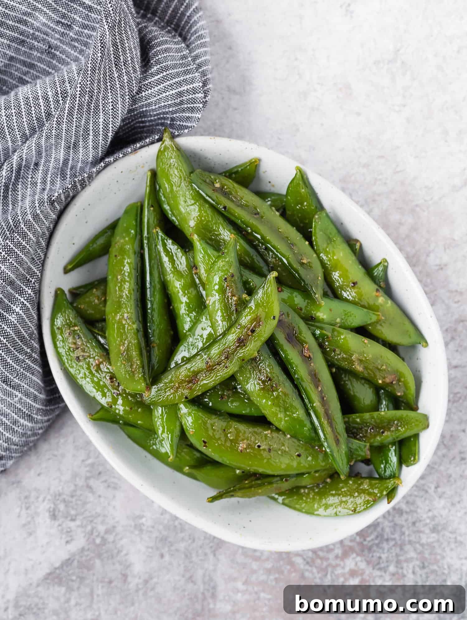 Crispy Roasted Sugar Snap Peas 7 White oval bowl with cooked snap peas in it, ready to be served.